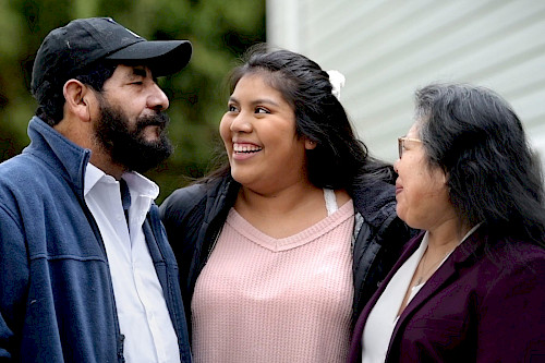 Three people standing together, with the two on the outside looking at the person in the middle