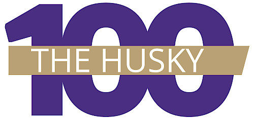 Image of the number 100 with a gold banner running through it and the words "The Husky" written in white on it